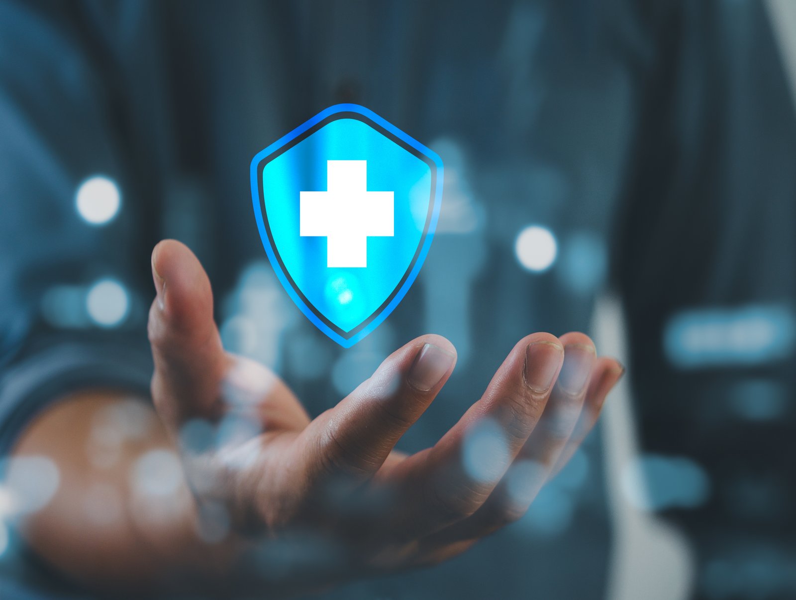 An open hand holding a glowing blue shield icon with a white medical cross symbol inside