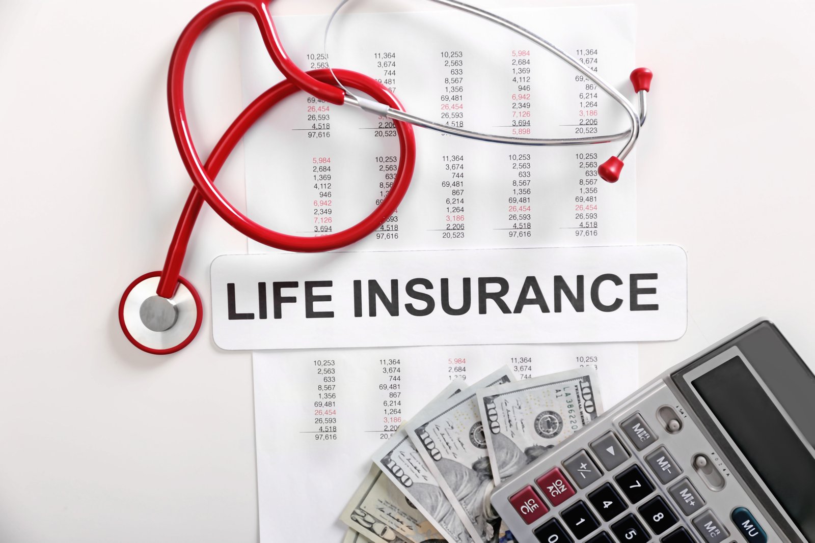 A red stethoscope wrapped around a sign reading LIFE INSURANCE over a data sheet, next to a calculator and hundred dollar bills